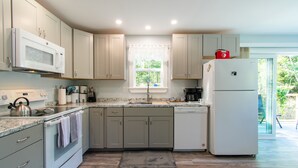 A modern kitchen with light-colored cabinets, a built-in microwave, a refrigerator, and a window providing natural light. - Intown Bar Harbor Home Owned by Local Family - Acadia Entrance Around the Corner (Bar Harbor)