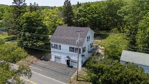 Une maison à deux étages avec un garage, entourée d’arbres et disposant d’un parking.