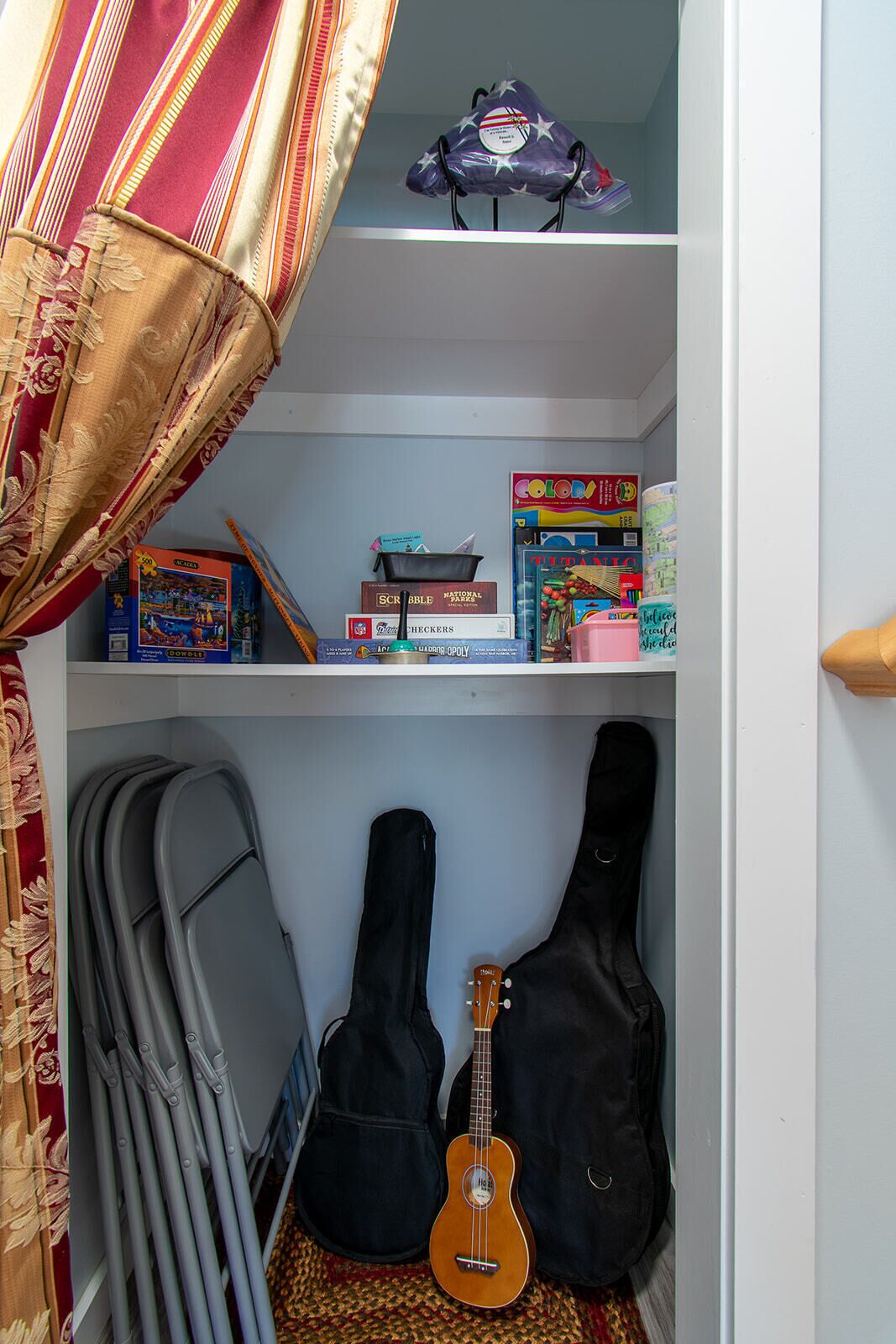 A closet with shelves containing board games, a guitar, and a ukulele.