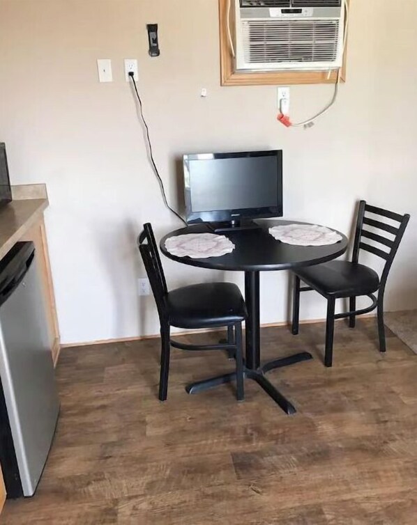Una cocina compacta con una mesa de comedor, dos sillas, un refrigerador y un equipo de aire acondicionado instalado en la pared.