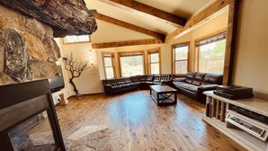 A spacious living room with a stone fireplace, wooden beams, a sectional sofa, and a built-in entertainment unit. - 3  🛌rooms in🐻Hot Tub🧖‍♀️ cold tank 🥶Theatre📽Library 📚Pool🎱BBQ🍔Games🎯🏀♠️🎤Gym💪 (Big Bear)