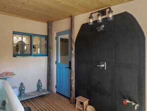 A bathroom with a wooden ceiling, a blue door, a shower with a black wall, and a small wooden stool. - Historic Adobe Casita with hot tub, fiber optic, and modern amenities (Taos)