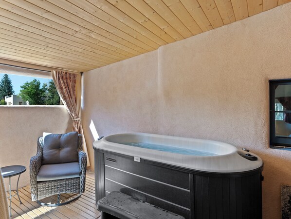 Un jacuzzi en una terraza de madera con una silla de mimbre y una pequeña mesa.