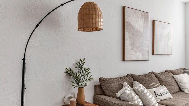 Una sala de estar moderna con un sofá marrón, una mesita de madera, una lámpara colgante de mimbre y dos cuadros abstractos en la pared.