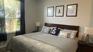 Une chambre à coucher avec un lit, un ventilateur de plafond, une fenêtre avec des rideaux et des tableaux encadrés accrochés au mur.