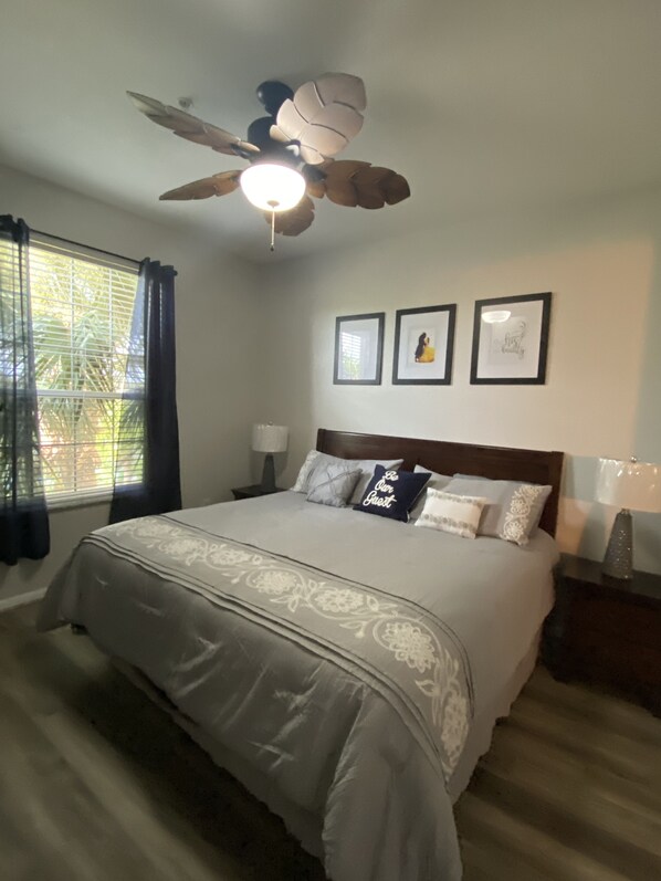 A bedroom with a bed, a ceiling fan, a window with curtains, and framed pictures on the wall. - Be our Guest - 3 bedroom, sleeps 7 + Condo w/ pool view by Disney and Universal (Kissimmee)