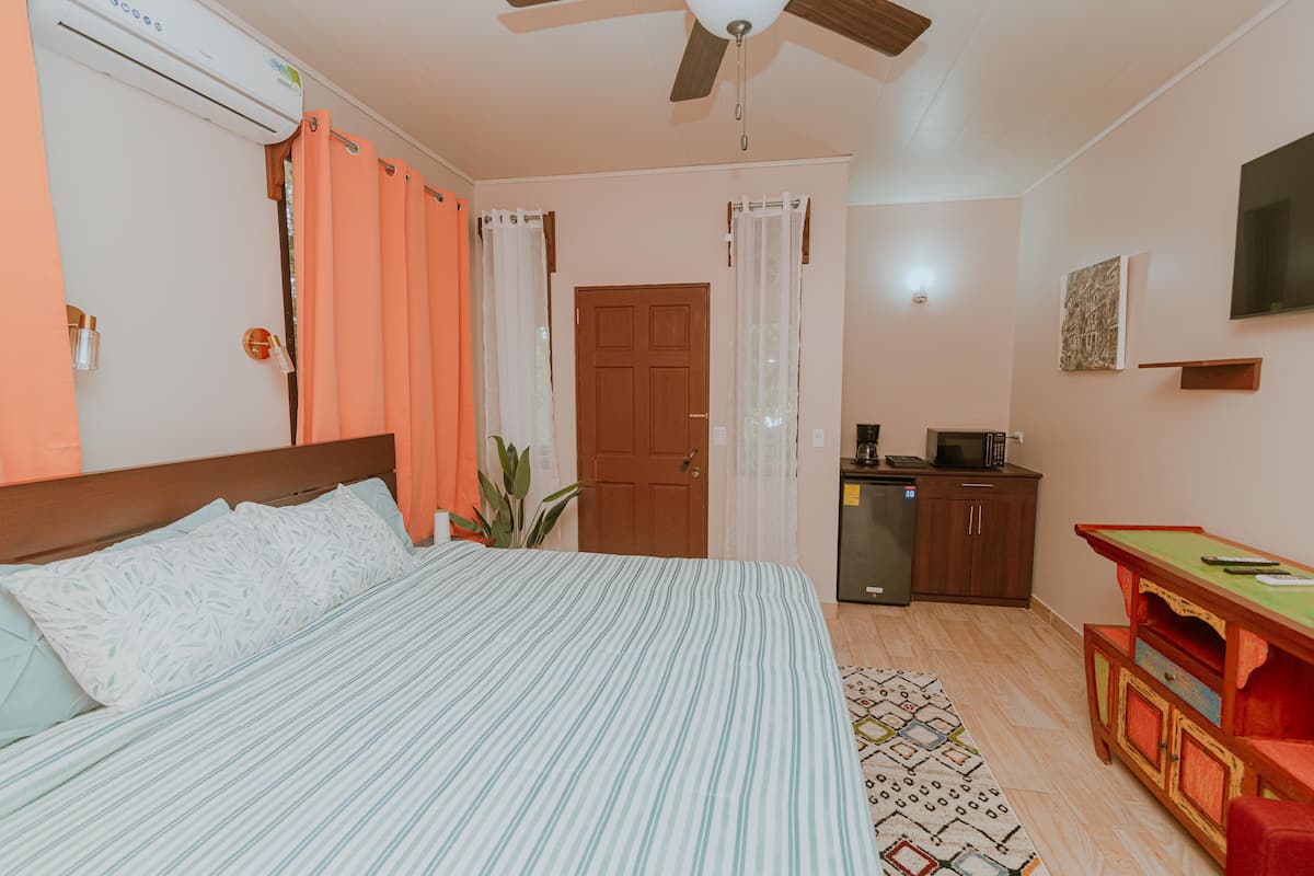Una habitación de hotel con cama, ventilador de techo, escritorio con silla, televisión y puerta.