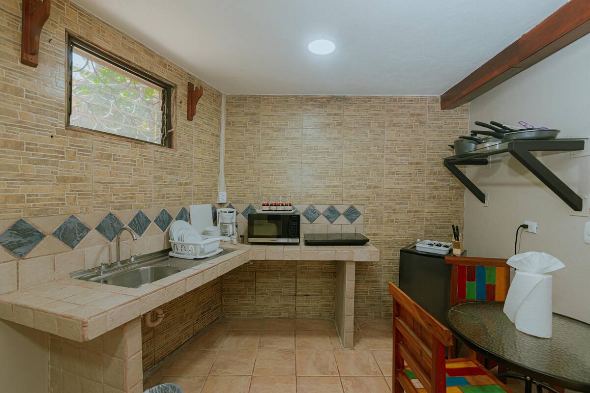 Una cocina compacta con lavamanos, microondas y un pequeño comedor con una silla y una mesa.