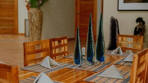 A wooden dining table with blue glass vases, wooden chairs, and blue and beige placemats. - Oasis Diverse Adult Retreat. (Quepos)