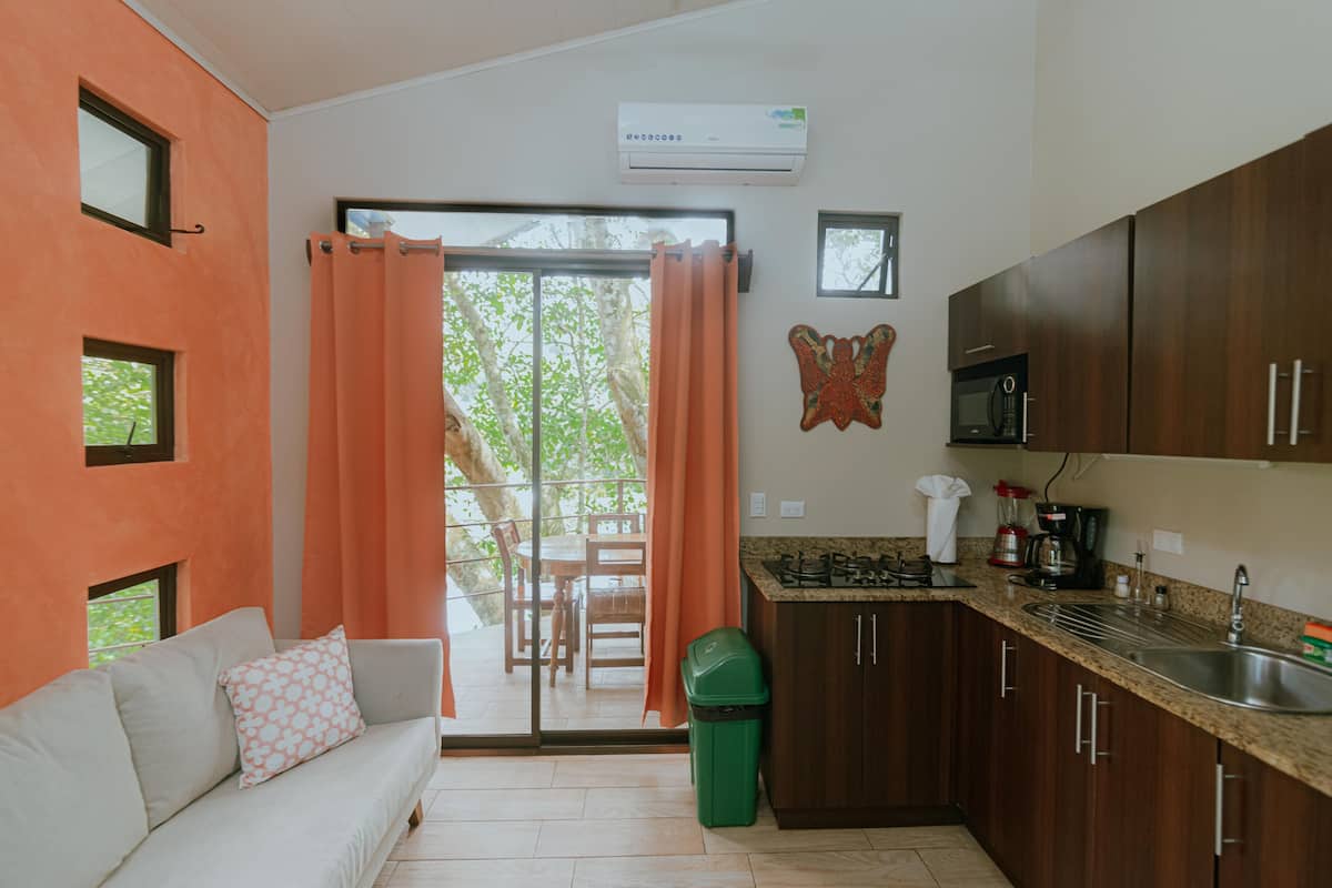 Una cocina moderna con microondas, fregadero y estufa, un comedor con mesa y sillas, y un ventanal corredero que da a un patio exterior.