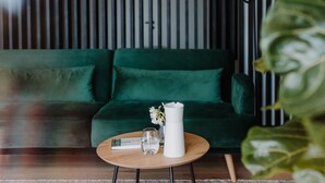 A modern living room with a green sofa, a round wooden coffee table, and a white vase with flowers. - Ruhiges Loft in der Natur mit Fantastischem Blick auf Meran (Dorf Tirol)