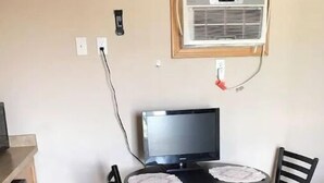 Eine kleine Küche mit Esstisch, zwei Stühlen, einem Kühlschrank und einer an der Wand montierten Klimaanlage.