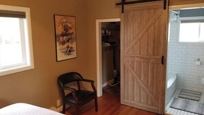 A bedroom with a bed, a chair, a wooden door, and a bathroom with a shower and a towel rack. - Cozy Hideaway with views of 3 Mountain Ranges (Clyde Park)