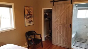 A bedroom with a bed, a chair, a wooden door, and a bathroom with a shower and a towel rack. - Cozy Hideaway with views of 3 Mountain Ranges (Clyde Park)