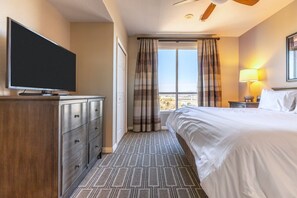 Een hotelkamer met een bed, een televisie op een dressoir, een raam met gordijnen en een lamp.