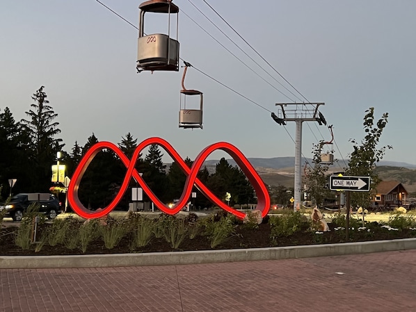 A red sculpture in a landscaped area with a 'One Way' sign and a cable car system in the background. - Hidden creek at Canyons Ski Resort (Park City)