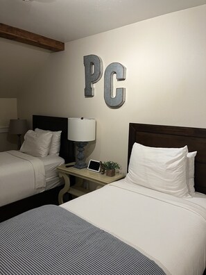 A hotel room with two beds, a nightstand with a lamp, a small table with a plant, and the letters "PC" on the wall. - Hidden creek at Canyons Ski Resort (Park City)