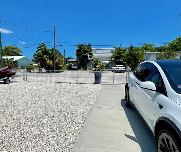 A white car parked on a gravel driveway with a metal fence and a building in the background. - Beautiful Modern House in Key Largo (Key Largo)