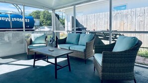 A covered outdoor seating area with wicker furniture and a table, overlooking a wooden fence and a clear sky. - Beautiful Modern House in Key Largo (Key Largo)