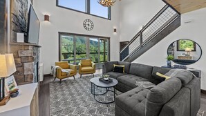 Un vaste espace de vie agrémenté d’une cheminée en pierre, de grandes fenêtres, d’un escalier et d’un coin salon confortable.
