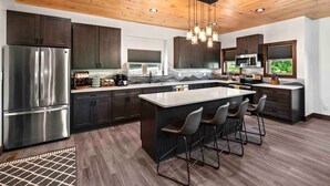 Une cuisine moderne avec des meubles de couleur sombre, des appareils en acier inoxydable, un îlot central doté de tabourets de bar et un plafond en bois.