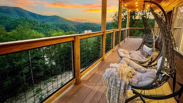 Une terrasse en bois avec un fauteuil suspendu et des sièges rembourrés, offrant une vue sur un paysage boisé.