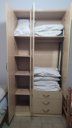 Un armario de madera con varios estantes y cajones, algunos con ropa de cama blanca.