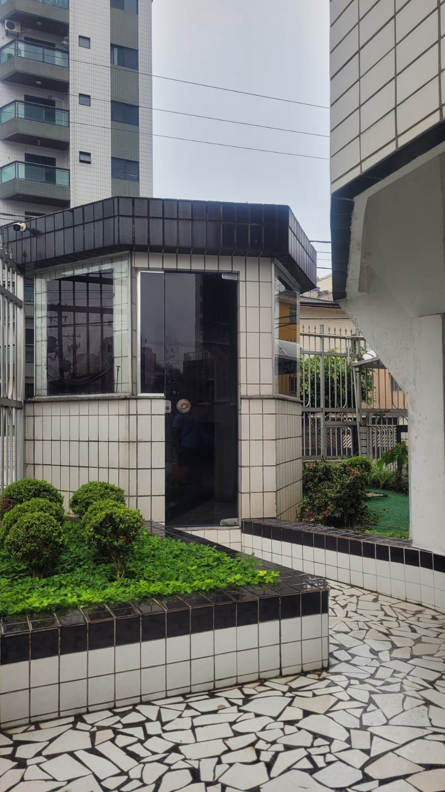 Edifici modern amb entrada enrajolada, una petita zona de jardí amb arbustos i un paviment enrajolat.