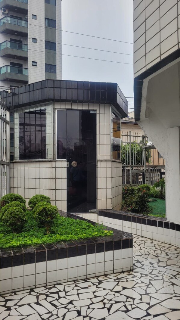 Un edificio moderno con entrada de baldosas, un pequeño jardín con arbustos y un suelo de baldosas.