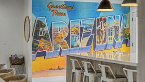 Un mural vibrante con el texto 'Greetings From ARIZONA!', una cesta tejida y una zona de bar con taburetes.