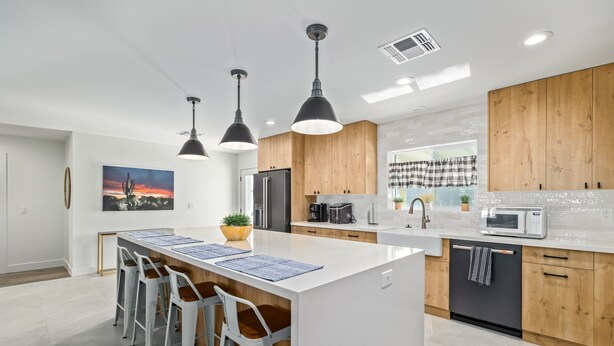 Una cocina moderna con una isla central, taburetes de bar, armarios de madera y un amplio ventanal con vistas.