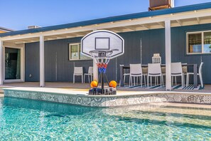A poolside area with a basketball hoop, outdoor seating, and a tiled pool.