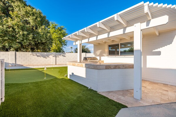A modern outdoor patio with a grill and a small putting green.