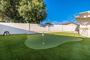 A backyard with artificial grass, a putting green, and a white wall.