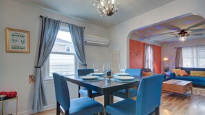 Un coin repas avec une table dressée pour quatre personnes, des chaises à l’assise rembourrée de couleur bleue et un lustre.