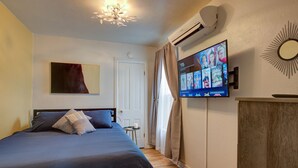 Une chambre à coucher avec un lit, un téléviseur fixé au mur, un luminaire au plafond et une porte.