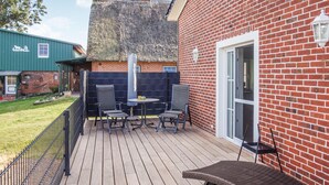 Eine Terrasse mit Tisch und Stühlen, eine Ziegelwand und eine strohgedeckte Struktur im Hintergrund.