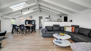 Un vaste espace de vie doté d’un haut plafond, une table à manger avec des chaises, un canapé et une table basse sur laquelle sont disposés des fruits.