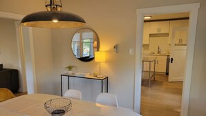 A dining area with a round table, chairs, a lamp, and a kitchen in the background.