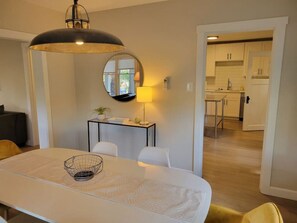 A dining area with a round table, chairs, a lamp, and a kitchen in the background.