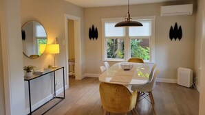A dining area with a round table, chairs, and a pendant light. There is a window with a view of greenery outside. - Modern Craftsman Garden Patio (Seattle)
