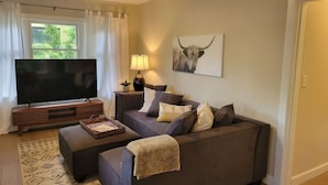 A modern living room with a large flat-screen TV, a sofa, a coffee table, and a lamp.