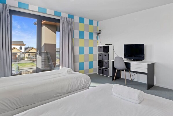 A hotel room with two beds, a desk with a TV, and a view of a building outside.