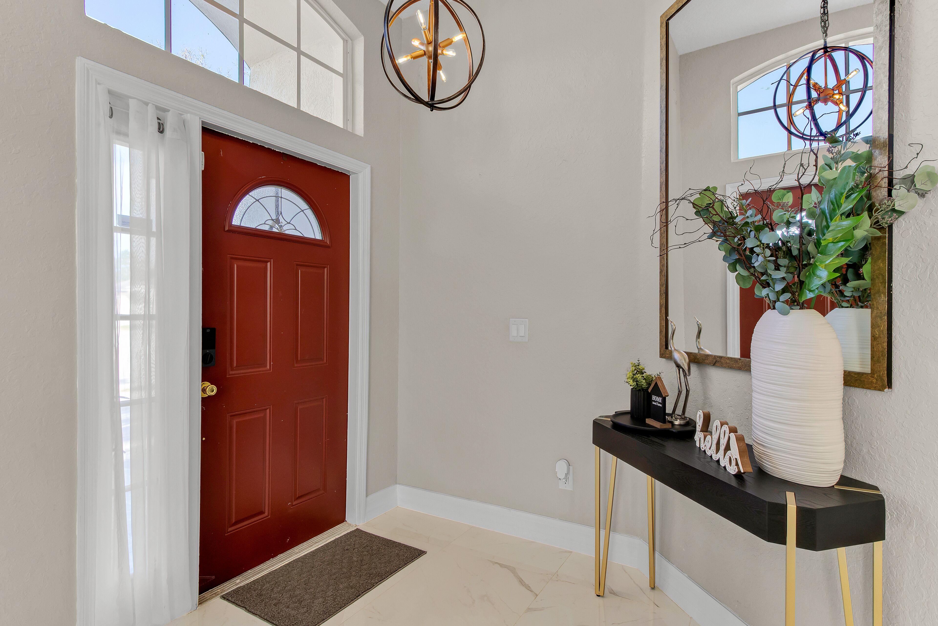 Une porte rouge avec un cadre blanc, une console noire ornée d’un miroir et un luminaire suspendu.