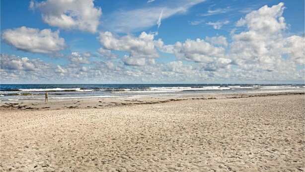 Een breed zandstrand met golven en een heldere lucht.