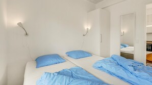 Een slaapkamer met twee bedden, elk voorzien van een blauw kussen, en een garderobe met spiegel.