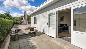Een wit huis met een terras, een houten tafel en een parasol.