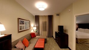 A hotel room with a sofa, a small table, a television, and a bed.