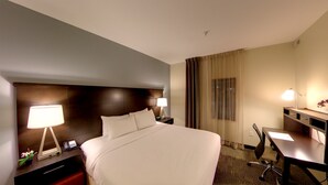 A hotel room with a large bed, bedside lamps, a desk with a chair, and a window with curtains.