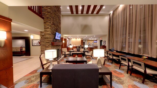 A hotel lobby with a stone accent wall, a TV mounted above a fireplace, and a dining area with tables and chairs.